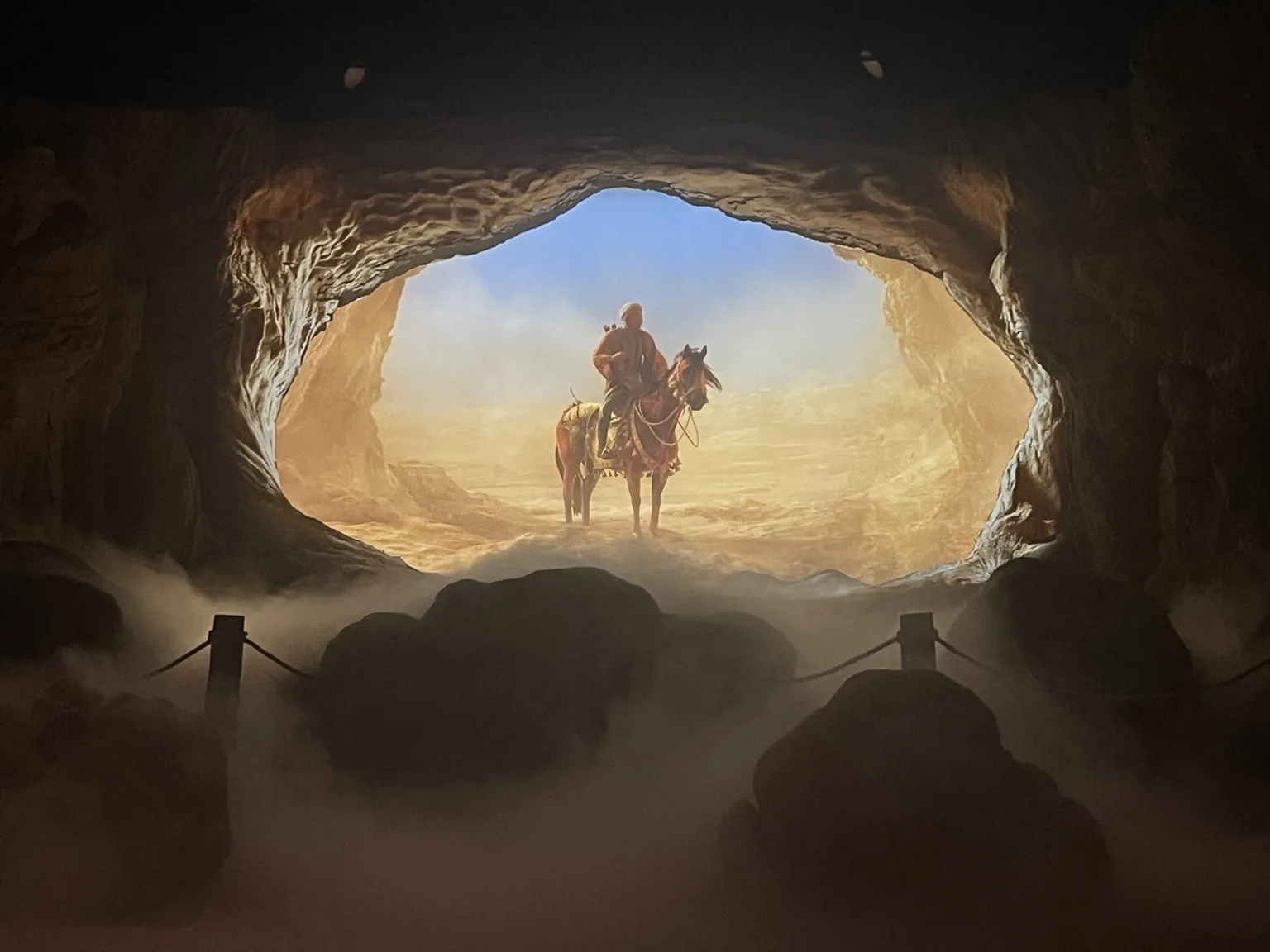 A projected desert scene with a rider, viewed through a scenic cave opening.