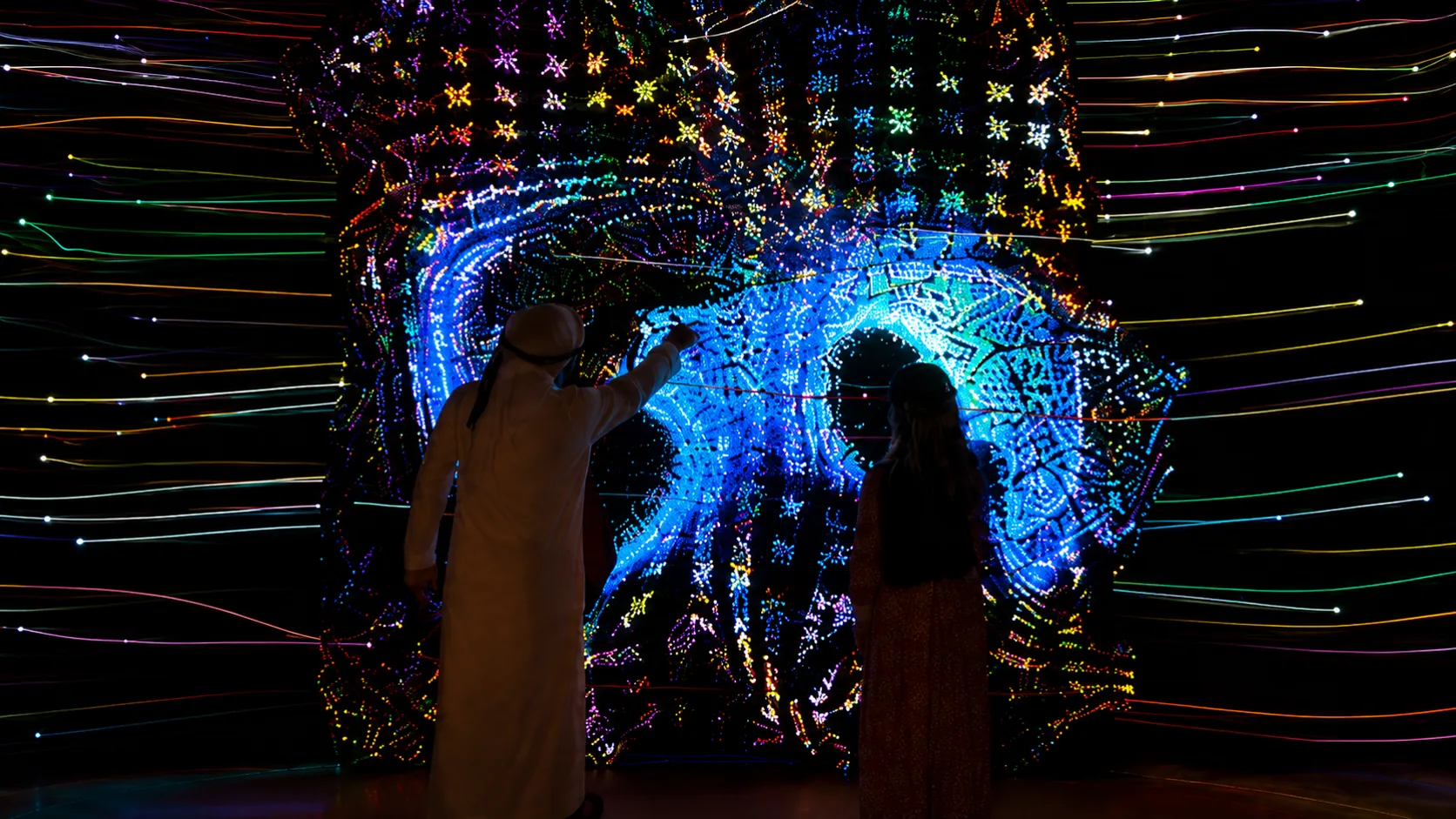 Visitors interacting with a large U-shaped generative media wall in the UAE.